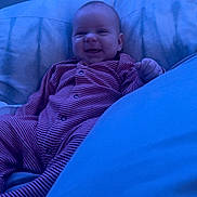 Jamie is registered to the contest to win money with this photo: baby, smiling, pajamas, bed, bedding, blue_tone, indoor, child, sleepwear, comfort, portrait, young_child, happy, cozy, relaxed, infant, cute, person, lying_down, soft_lighting