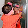 Miral is registered to the contest to win money with this photo: child, toddler, reflection, mirror, orange_dress, headband, flower, bracelets, colorful, curious, indoor, portrait, cute, baby, person, looking, playful, young_child, face, closeup