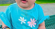 Miral is registered to the contest to win money with this photo: baby, toddler, child, outdoor, picnic_table, headband, flower, bracelets, blue_shirt, pants, grass, trees, park, face, sitting, curious, colorful, cute, person, daylight