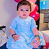 Miral is registered to the contest to win money with this photo: baby, child, blue_dress, bangles, balloons, pony_tail, sitting, foot, indoor, ottoman, furniture, colorful, cute, celebration, portrait, smiling, decor, room, lamp, happy