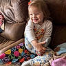 child, toddler, smiling, couch, blanket, colorful, peace_sign, pajamas, foot, hugging, indoor, cozy, leather, happy, girl, home, casual, playful, seated, relaxed
