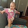 toddler, child, baby, smiling, happy, portrait, indoor, armchair, blanket, home, living_room, clothing, pink_shirt, cartoon, standing, arms_outstretched, blonde_hair, face, furniture, photography