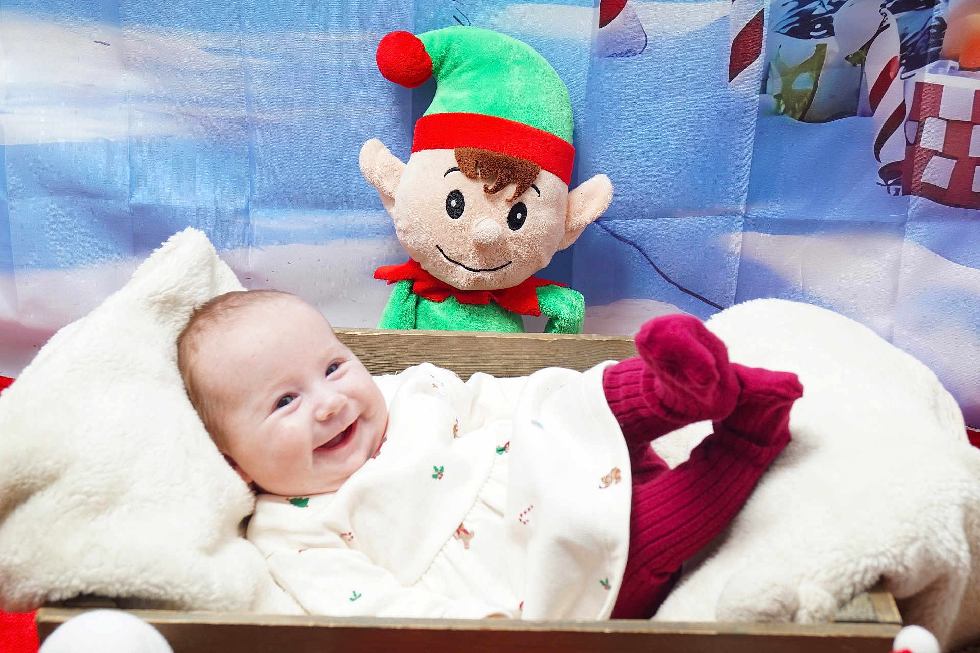 Lily joined the competition — help win amazing prizes! baby, infant, smiling, plush_toy, elf, holiday, christmas, festive, blanket, wooden_box, red_socks, cozy, cute, indoor, portrait, happy, decor, child, toy, background