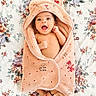 baby, smiling, towel, hooded_towel, teddy_bear, floral, bedspread, infant, cute, happy, wrapped, soft, cozy, child, small, feet, face, lying_down, expressive, blanket