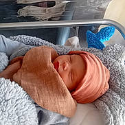 Damon a rejoint le concours — aidez-le/la à gagner de superbes lots ! newborn, baby, sleeping, blanket, hat, hospital, bassinet, soft_toy, cozy, infant, child, cute, resting, wrapped, knitted, blue, pink, fabric, peaceful, indoor