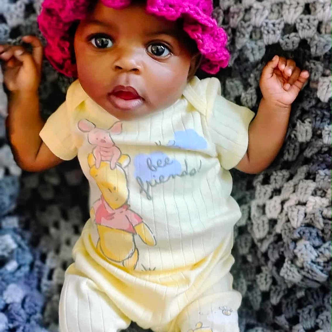 Rere is registered to the contest to win money with this photo: baby, child, cozy, curious, cute, face, gray_blanket, hands, hat, indoors, infant, knitted_blanket, lying_down, pajamas, pink_hat, portrait, smiling, soft_texture, winnie_the_pooh, yellow_clothing