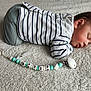 newborn, baby, sleeping, striped_clothing, pacifier, beads, carpet, soft_texture, infant, cute, peaceful, lying_down, indoors, child, small, resting, face, hand, footwear, cozy