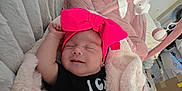 Emmeline is registered to the contest to win money with this photo: baby, infant, blanket, bow, headband, smile, sleeping, cushion, toy, pink, black_clothing, earrings, soft_texture, indoor, cozy, child, cute, resting, home, comfort