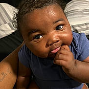 Khoa is registered to the contest to win money with this photo: baby, infant, child, face, eyes, cheeks, hand, fist, onesie, clothing, skin, portrait, closeup, smile, bed, pillow, adult_arm, tattoo, indoor, cute