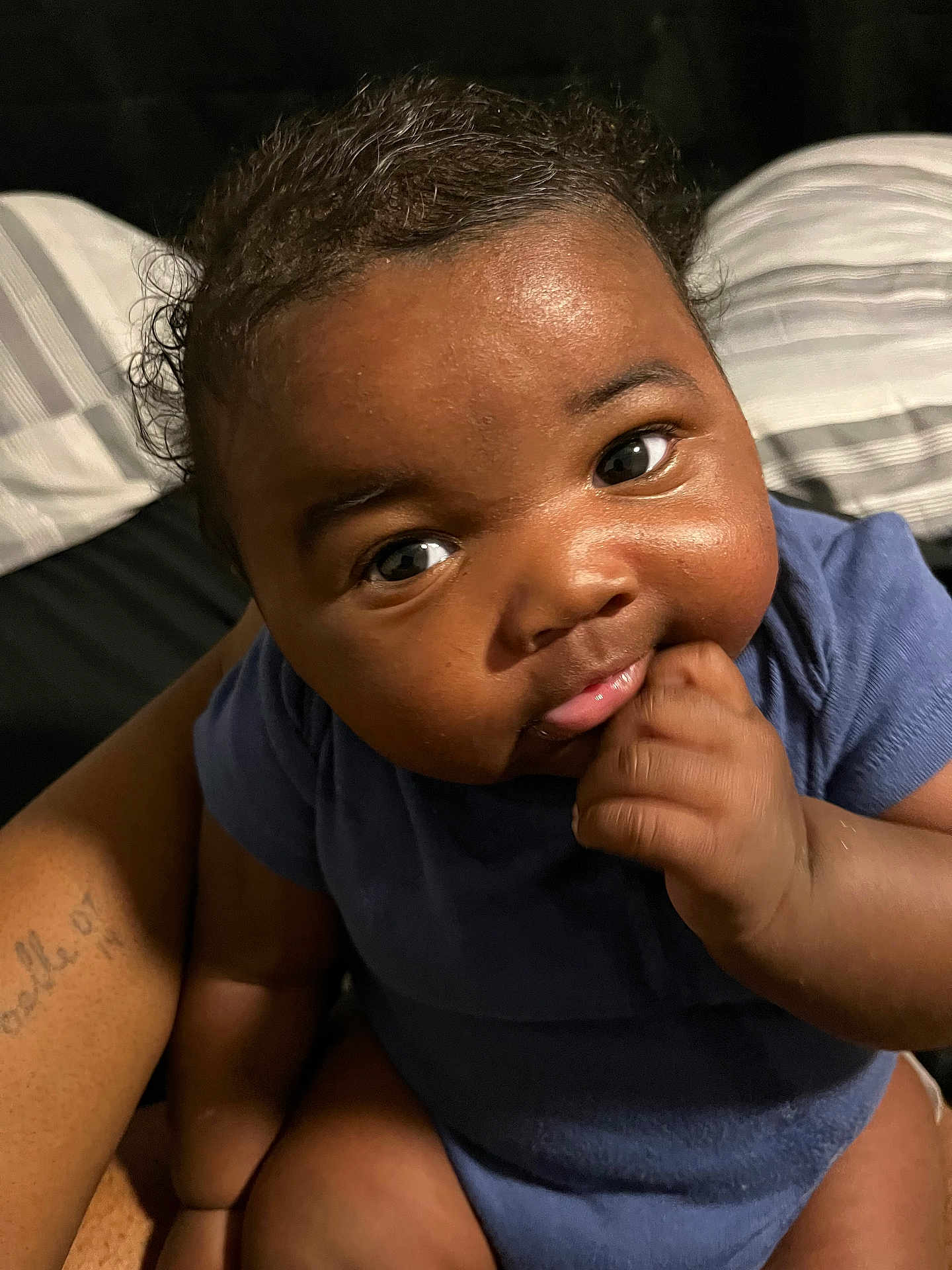 Khoa is registered to the contest to win money with this photo: baby, infant, child, face, eyes, cheeks, hand, fist, onesie, clothing, skin, portrait, closeup, smile, bed, pillow, adult_arm, tattoo, indoor, cute