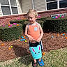 child, boy, outdoor, grass, bushes, easter_eggs, bucket, bunny, tank_top, slippers, spring, holiday, playing, happy, daylight, window, house, brick_wall, hedge, fun
