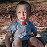 child, toddler, boy, outdoor, sand, leaves, sunlight, shadow, blue_eyes, bow_tie, short_sleeves, patterned_clothing, sitting, nature, expression, face, legs, grass, daylight, casual