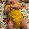 baby, infant, yellow_onesie, smiling, lying_down, blanket, animal_print, face, legs, feet, baby_supplies, basket, happy, child, person, cute, indoors, soft_lighting, newborn, resting