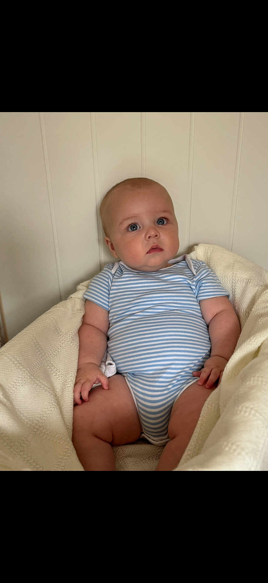 Teddy joined the competition — help win amazing prizes! baby, infant, child, blue_eyes, striped_onesie, knitted_blanket, cozy, cute, chubby, sitting, indoor, soft_light, neutral_background, portrait, face, skin, hand, leg, expression, young
