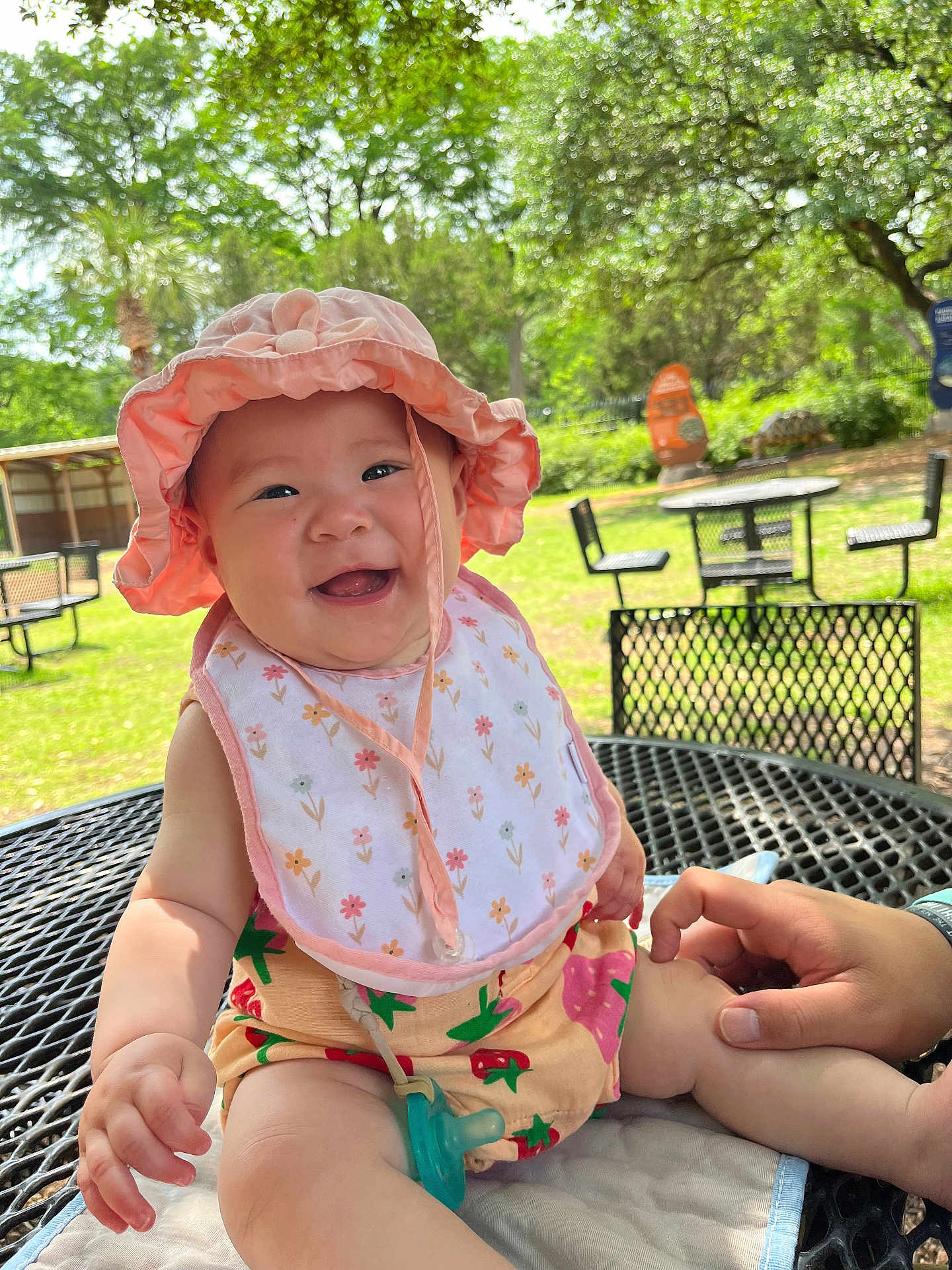 Himari joined the competition — help win amazing prizes! baby, child, smiling, hat, bib, pacifier, hand, outdoor, table, chair, park, greenery, sunlight, happy, infant, clothing, person, nature, metal, summer