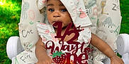 Khwezi is registered to the contest to win money with this photo: baby, infant, child, highchair, face, bonnet, hat, cake_topper, strawberry, dragonfruit, orange_slice, plate, hand, outdoor, grass, patterned_cushion, cute, celebration, portrait, photography