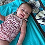 baby, infant, smiling, towel, floral_onesie, cute, happy, skin, arm, hand, face, head, laying_down, pattern, textile, blue_towel, background, closeup, portrait, child