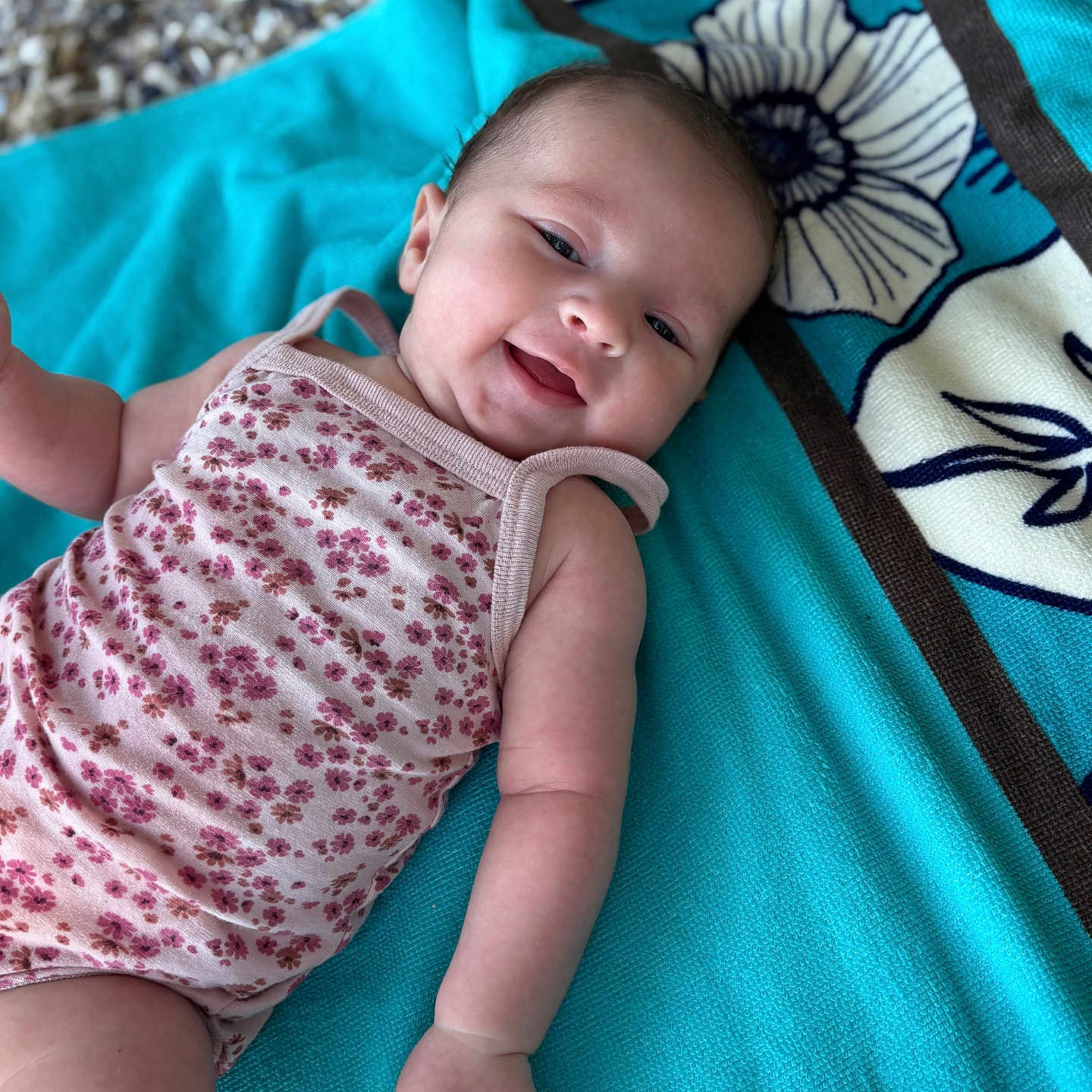 Alix participe au concours pour gagner de l'argent avec cette photo : arm, baby, background, blue_towel, child, closeup, cute, face, floral_onesie, hand, happy, head, infant, laying_down, pattern, portrait, skin, smiling, textile, towel