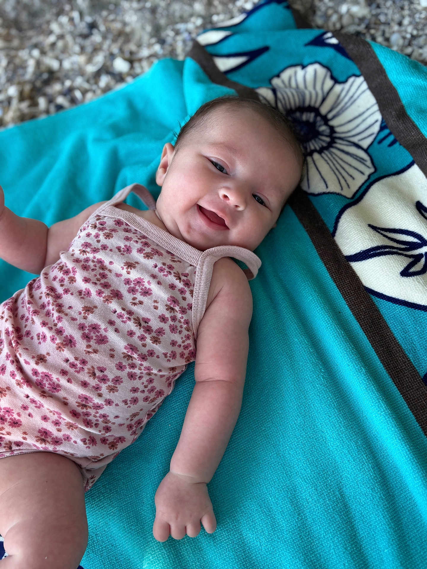 Alix participe au concours pour gagner de l'argent avec cette photo : baby, infant, smiling, towel, floral_onesie, cute, happy, skin, arm, hand, face, head, laying_down, pattern, textile, blue_towel, background, closeup, portrait, child