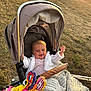 Lottie is registered to the contest to win money with this photo: baby, stroller, blanket, toy, outdoor, grass, sunlight, happy, smile, child, knitwear, colorful, plush_toy, nature, warm_light, person, infant, seat, relaxation, playful