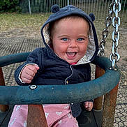 Lottie is registered to the contest to win money with this photo: baby, child, swing, playground, hooded_jacket, blue_eyes, smiling, happy, outdoor, grass, metal_chain, rust, pink_pants, animal_print, fist, seat, person, infant, cute, joyful