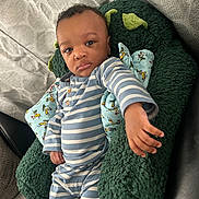 Jacai is registered to the contest to win money with this photo: baby, child, pajamas, striped_clothing, cushion, pillow, green, blue, indoor, furniture, sofa, person, cute, infant, hand, face, expression, relaxed, plush, casual