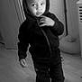 child, boy, hoodie, black_and_white, indoor, floor, wooden_floor, pants, shoes, standing, thoughtful, casual_clothing, young_child, portrait, expression, hand, person, monochrome, home, cozy