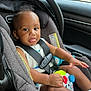 baby, car_seat, child, toy, car_interior, seatbelt, playful, infant, smiling, cute, sitting, clothing, safety, colorful, hand, face, head, window, vehicle, seat