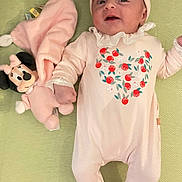 Gabriela participe au concours pour gagner de l'argent avec cette photo : baby, infant, pink_outfit, hat, booties, strawberry_pattern, plush_toy, minnie_mouse, pacifier, green_surface, cute, smiling, lying_down, indoor, child, person, soft_toy, sleepwear, adorable, cozy