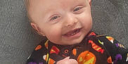 Able is registered to the contest to win money with this photo: baby, smiling, child, infant, face, clothing, onesie, halloween, pumpkin, candy_corn, bat, colorful, cute, happy, teeth, hand, fist, lying_down, texture, gray_background
