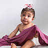 Sienna is registered to the contest to win money with this photo: baby, blanket, child, curious_expression, cute, diaper, headwear, indoor, infant, one_child, pink_bow, playful, portrait, purple_blanket, sitting, smiling, soft_lighting, studio, white_background, young_child