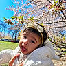 baby, blue_sky, cherry_blossom, child, cute, face, flower, green_grass, hand, headband, jacket, nature, outdoor, park, person, portrait, smiling, spring, sunny, tree