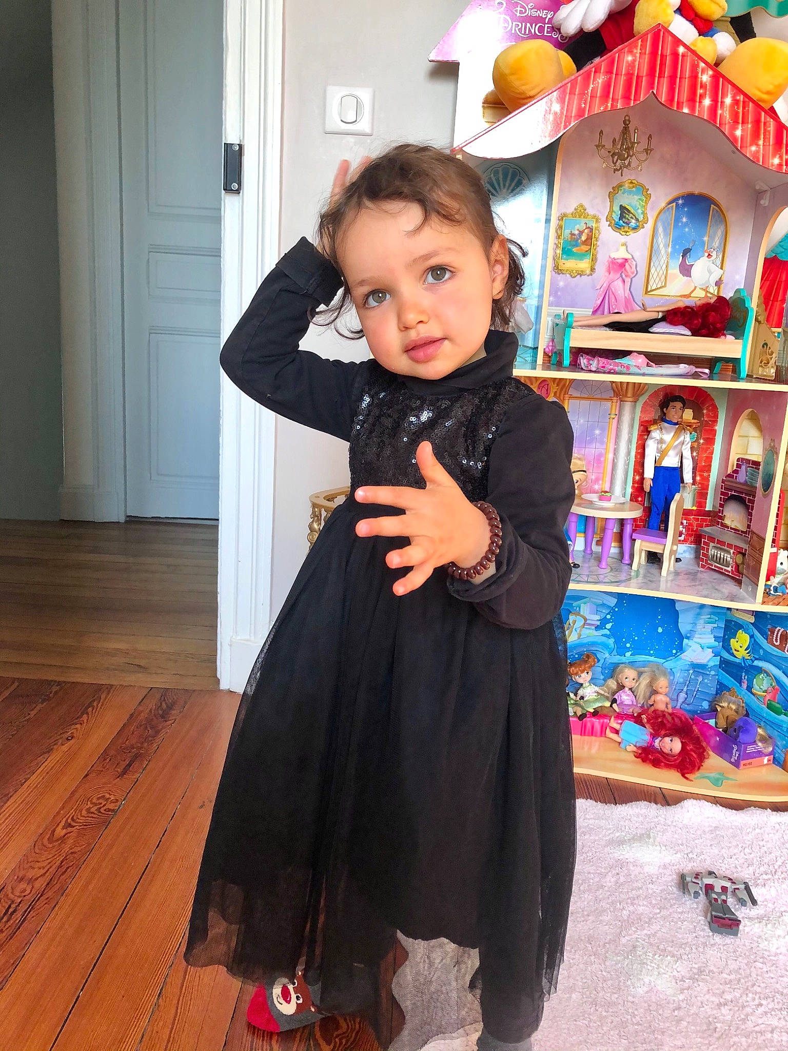 Emma participe au concours pour gagner de l'argent avec cette photo : baby, baby_toddler_clothing, child, door, event, fashion_design, flooring, formal_wear, fun, happy, hardwood, person, room, shelf, shelving, sleeve, toddler, toy, varnish, wood