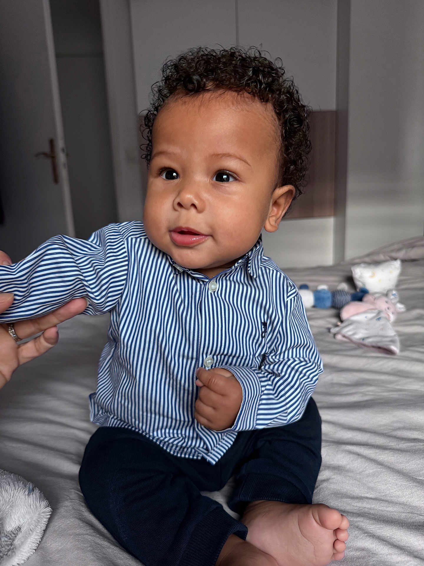 Kaïzen a rejoint le concours — aidez-le/la à gagner de superbes lots ! toddler, child, curly_hair, striped_shirt, dark_pants, bed, soft_toys, hand, foot, indoors, person, smiling, cute, baby, portrait, sitting, skin, clothing, room, furniture
