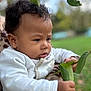 baby, child, curly_hair, outdoor, green_leaves, nature, hand, face, portrait, closeup, focus, expression, person, clothing, holding, adult, skin, background_blur, daylight, serious