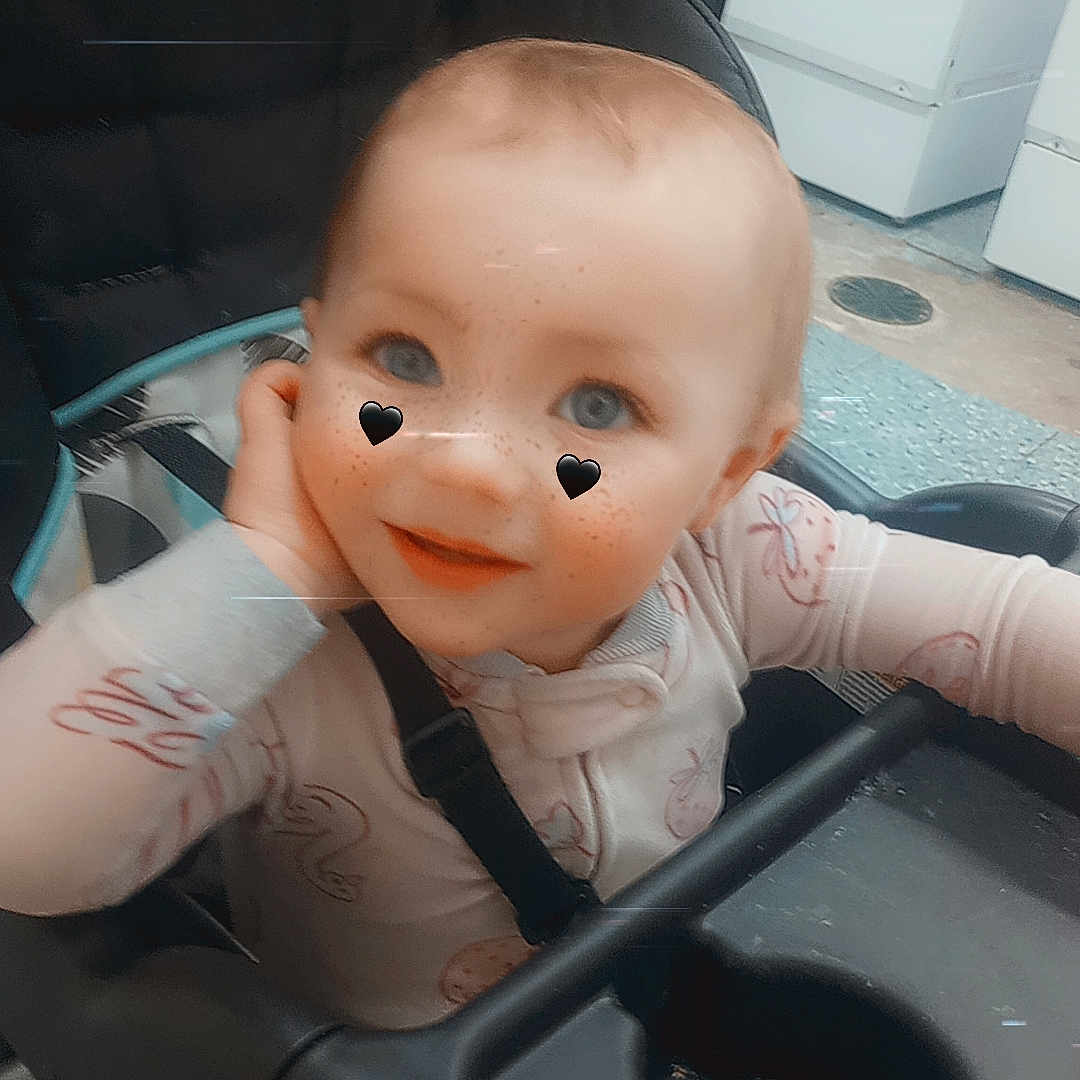 Raelinn is registered to the contest to win money with this photo: baby, child, stroller, onesie, face, blue_eyes, heart_stickers, indoor, washing_machine, home, seatbelt, tray, curious, smile, head, hand, furniture, floor, cute, infant