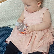 Raelinn joined the competition — help win amazing prizes! baby, child, dress, pink, black_leggings, water_bottle, sitting, indoor, curious, patterned_cushion, blue, soft_fabric, infant, cute, portrait, young_child, holding_object, side_profile, light_skin, short_hair