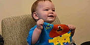 Simon joined the competition — help win amazing prizes! toddler, child, high_chair, blue_shirt, cartoon_characters, table, wooden_table, indoor, smiling, happy, person, baby, furniture, seated, cute, young_child, cheerful, casual_clothing, face, raising_hands