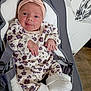 baby, infant, headband, floral_outfit, baby_seat, cushion, white_socks, cute, newborn, portrait, indoors, comfort, seatbelt, child, soft_texture, clothing, smile, person, resting, curious