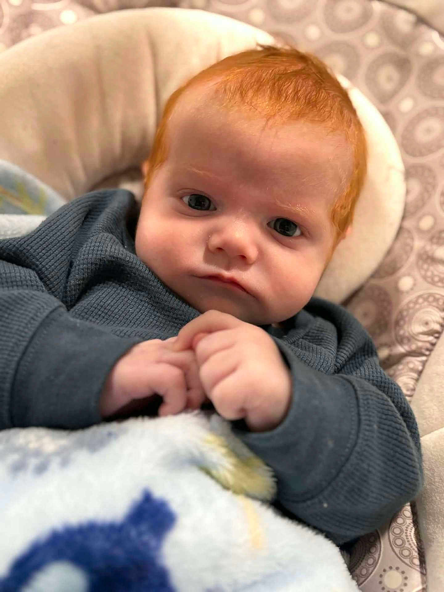 Hayden Roker is registered to the contest to win money with this photo: baby, redhead, infant, face, hands, blanket, clothing, sweater, cushion, pattern, portrait, indoor, child, young, closeup, resting, expression, cozy, cute, skin
