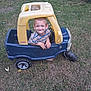 child, toy_car, grass, outdoor, smiling, play, young, boy, plastic, vehicle, barefoot, lawn, casual_clothing, striped_shirt, fun, happy, nature, small, playground, daylight