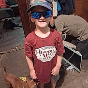 Kylo is registered to the contest to win money with this photo: child, boy, hat, sunglasses, tshirt, barefoot, dog, indoor, person, monitor, floor, casual, smile, reflection, clothing, pet, animal, room, candid, curious