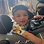 Siwaÿn participe au concours pour gagner de l'argent avec cette photo : baby, child, smiling, cap, toy, steering_wheel, indoor, floor, tile, clothing, person, cute, happy, play, infant, seat, foot, hand, cartoon_print, young