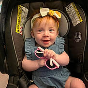 Willow is registered to the contest to win money with this photo: baby, child, car_seat, headband, pink_sunglasses, smile, happy, infant, blue_outfit, seatbelt, indoors, cute, young_child, person, holding, accessory, playful, closeup, adorable, skin