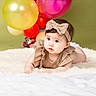baby, child, infant, cute, headband, bow, balloons, fluffy_rug, white_blanket, beige_clothing, portrait, smiling, curious, studio, indoor, soft_lighting, colorful, decor, young, crawling