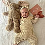 baby, infant, knitted_clothing, headband, stuffed_animal, bunny, toy, milestone_card, blanket, soft_texture, lying_down, hand, foot, cute, smile, face, child, indoor, portrait, laying