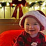 Selena is registered to the contest to win money with this photo: baby, child, smiling, santa_hat, red_plaid, holiday, christmas, festive, lights, bow, indoors, cute, happy, portrait, face, warm_lighting, seasonal, celebration, cozy, infant