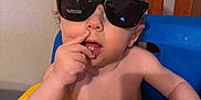 Liam joined the competition — help win amazing prizes! toddler, child, sunglasses, high_chair, yellow_tray, shirtless, indoor, furniture, wooden_chair, curly_hair, messy, cute, baby, hand, face, expression, mouth, skin, person, seat