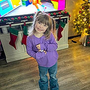 Raylee is registered to the contest to win money with this photo: child, girl, pigtails, smiling, purple_shirt, jeans, brown_shoes, living_room, christmas_tree, stockings, flooring, cabinet, television, holiday_decor, ornaments, festive, home_interior, happy, person, cute