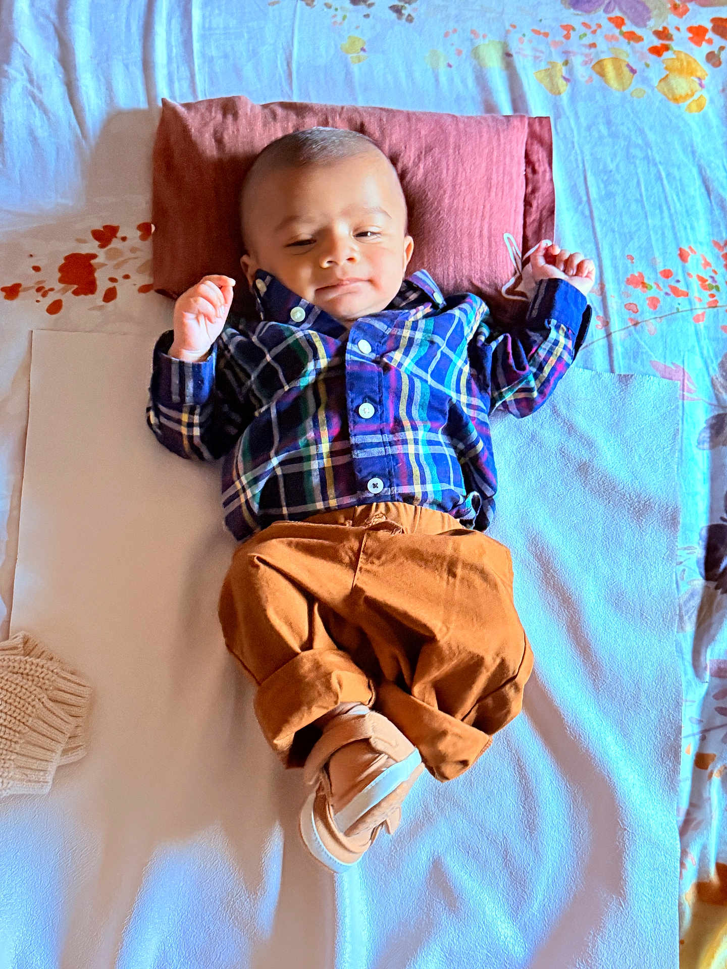 Trishiv is registered to the contest to win money with this photo: baby, infant, plaid_shirt, brown_pants, pillow, bed, blanket, footwear, sleepwear, child, relaxing, indoors, cute, portrait, smiling, person, young, cozy, comfortable, sleepy